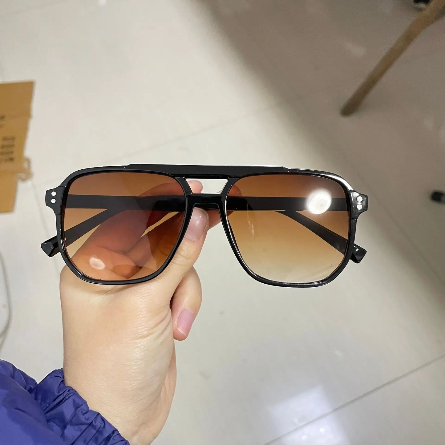 Hand holding Vintage Men Women Big Sunglasses Men Square Shades Brand Designer Unisex Sun Glasses Black Lense Male Female Sunglasses UV400 with large square amber-tinted lenses and black frame.